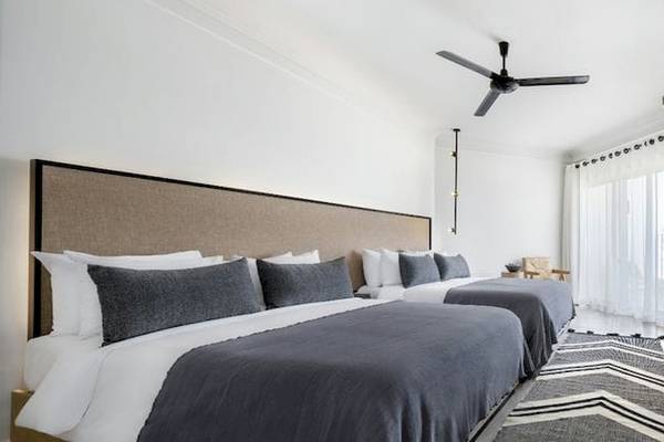 Zwei moderne Schlafzimmer im Serry Beach Resort mit weißen Wänden, Deckenventilator, Fernseher und Bettwäsche.