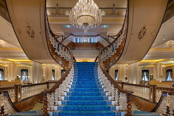 Innenansicht des Treppenhauses im Titanic Mardan Palace mit blauen Teppichen und einem großen Kristallkronleuchter.