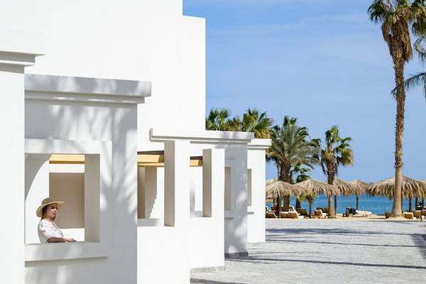 Eine Frau in einem weißen Gebäude des Serry Beach Resorts blickt aus dem Fenster auf den Strand und die Palmen.