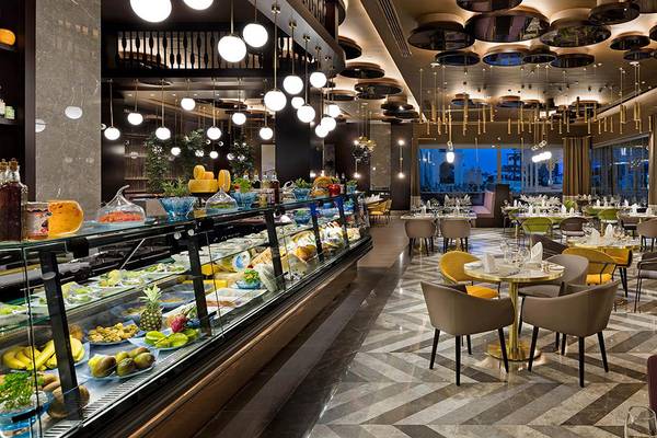 Innenansicht des Restaurants des Titanic Mardan Palace Hotels mit vielen Tischen und Stühlen, einer großen Auswahl an Gerichten und hängenden Kronleuchtern.