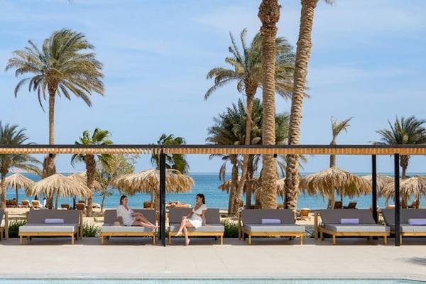 Zwei Frauen sitzen auf Lounge-Sesseln im Freien neben einem Pool, mit Blick auf das Meer und Palmen im Hintergrund, im Serry Beach Resort.
