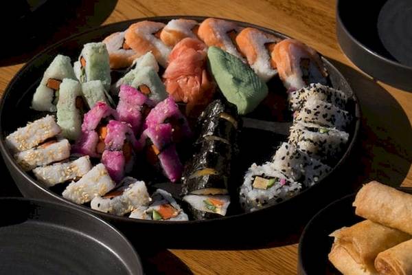 Ein großer Teller mit verschiedenen Sushi-Rollen und Springrollen auf einem Holztisch.