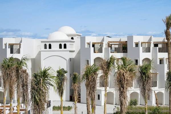 Außenansicht des weißen Serry Beach Resorts mit mehreren Stockwerken und Palmen davor.