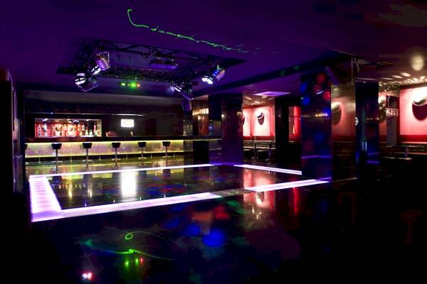Nachtclub mit farbigen Lichtern und einer Bar im Hintergrund.