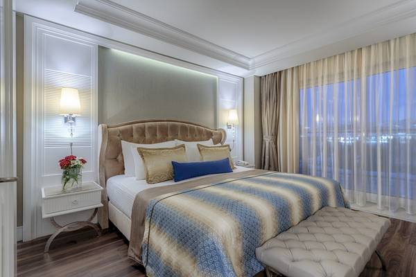 Schlafzimmer im Dobedan Exclusive Hotel & Spa Belek mit Bett, Nachttisch, Fenstern und Dekoration.