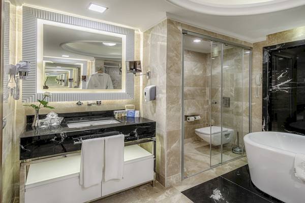 Badezimmer im Dobedan Exclusive Hotel & Spa Belek mit Marmorboden und -wänden, Glasdusche, Badewanne und Waschbecken.