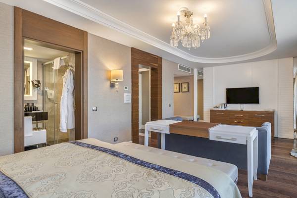 Schlafzimmer im Dobedan Exclusive Hotel & Spa Belek mit Bett, Couch, Fernseher und Kristallleuchter.