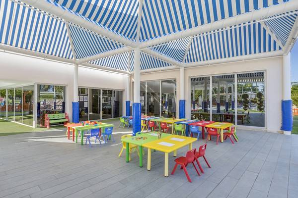 Farbig gestalteter Spielplatzbereich im Dobedan Hotel mit bunten Tischen und Stühlen unter einer blau-weiß gestreiften Markise.