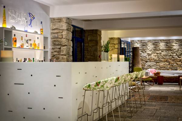 Barbereich des Mykonos Theoxenia Boutique Hotels mit weißen Barhockern und Steinwänden.