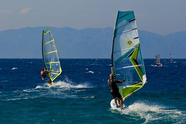 Mehrere Windsurfer segeln im Ozean vor einer Bergkulisse.