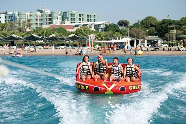 Vier Personen sitzen auf einem roten Schlauchboot und werden am Strand gezogen, vor dem Limak Atlantis Deluxe Hotel & Resort.