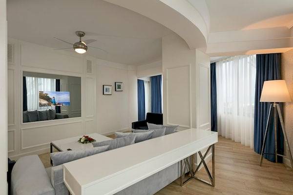 Hotelzimmer-Innenraum mit weißem Sofa, Tisch, Fernseher, Lampe und Holzboden.