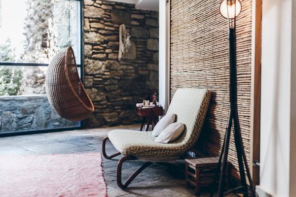 Inneneinrichtung des Mykonos Theoxenia Boutique Hotels mit einem Korbstuhl, Kissen, Tisch und Lampen.