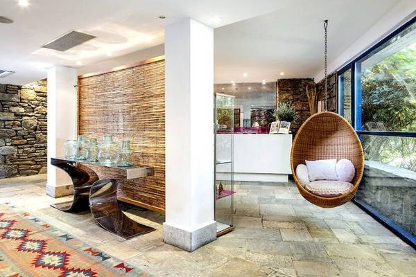 Innenbereich des Mykonos Theoxenia Boutique Hotels mit einem hängenden Korbstuhl und einem Steinwanddesign.