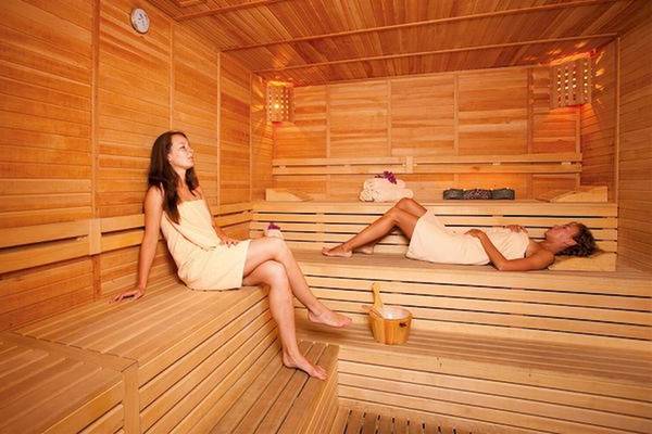 Zwei Frauen sitzen in einem Holzsauna, eine entspannt sich und die andere schaut zur Seite.