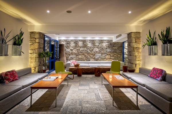 Innenbereich des Mykonos Theoxenia Boutique Hotels mit Steinwand, Sofas, Tischen und Pflanzen.