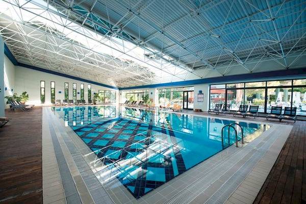 Innenansicht des Schwimmbades im Limak Atlantis Deluxe Hotel & Resort mit Liegestühlen und Glaswänden.