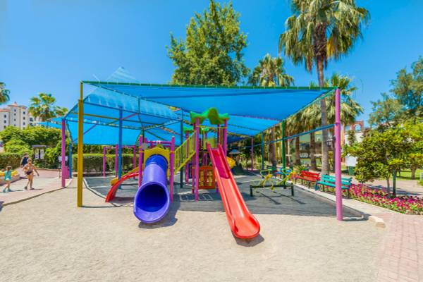 Kinderspielplatz im Freien im VONRESORT Golden Beach unter einem blauen Sonnensegel.