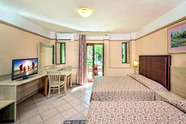 Innenansicht eines Zimmers im VONRESORT Golden Beach Hotel mit zwei Betten, Schreibtisch und Fernseher.