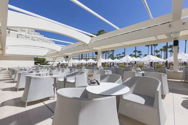 Außenterrasse des Hipotels Mediterraneo Hotels mit weißen Stühlen und Tischen unter Schirmen.