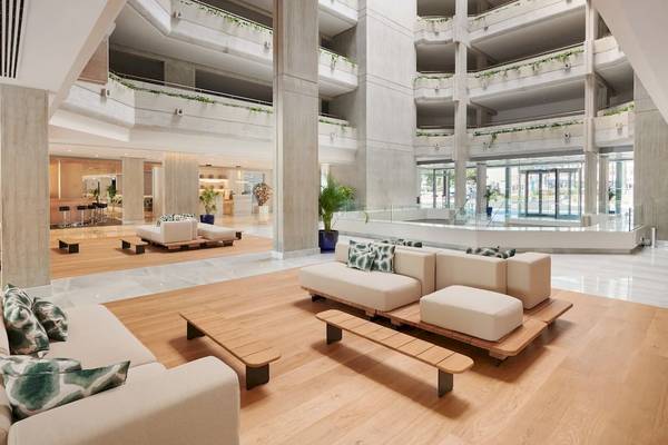Lobby des Hipotels Mediterraneo mit Sofas, Tischen und einem Swimmingpool im Hintergrund.