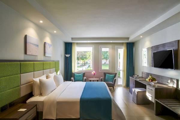 Innenansicht eines Schlafzimmers im Maritim Jolie Ville Resort & Casino Sharm El Sheikh mit Doppelbett, zwei Sesseln, Fernseher und Schreibtisch.
