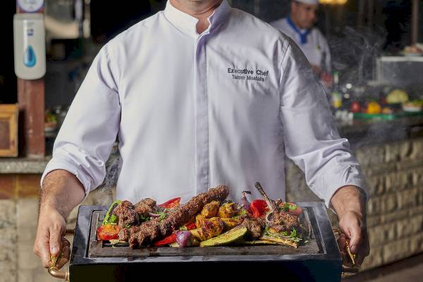 Executive Chef Tamer Mostafa hält eine Grillplatte mit verschiedenen gegrillten Gerichten.