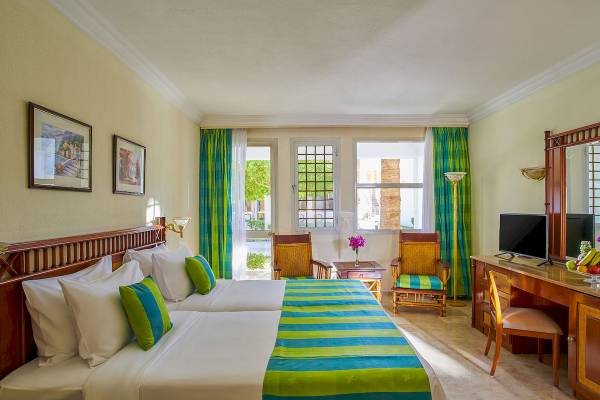 Doppelbettzimmer im Maritim Jolie Ville Resort & Casino mit zwei Betten, zwei Stühlen und einem Schreibtisch.