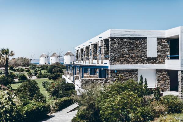 Außenansicht des Mykonos Theoxenia Boutique Hotels mit Steinmauern und blauen Fensterläden.