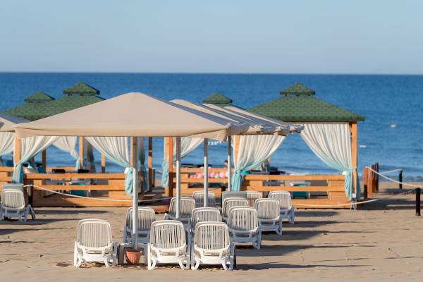 Sandstrand mit Sonnenschirmen und Lounge-Stühlen vor einem Hotelgebäude