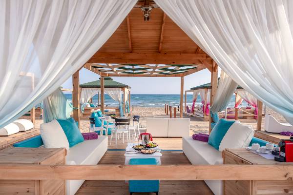 Lounge-Bereich am Strand des Sentido Kamelya Selin Hotels mit weißen und blauen Möbeln und weißen Vorhängen.