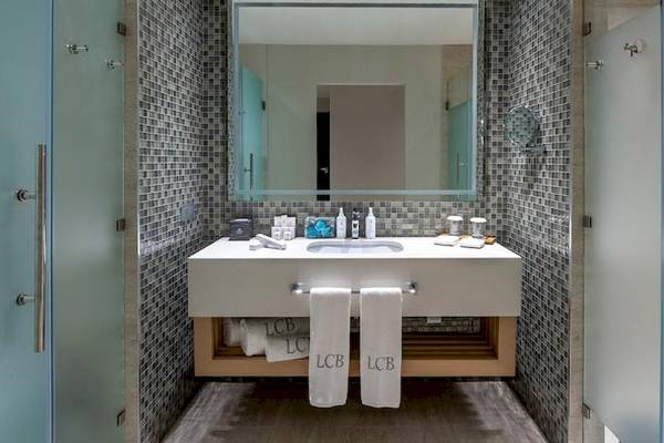 Badezimmer im Lopesan Costa Bavaro Resort Spa & Casino mit weißem Waschbecken, Spiegel und blauen Kacheln.