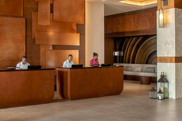 Rezeption im Lopesan Costa Bavaro Resort Spa & Casino mit drei Mitarbeitern hinter den Schreibtischen und einer Couch im Hintergrund.