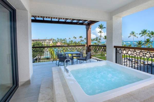 Ein Balkon mit einem Whirlpool und Blick auf das Meer, umgeben von Palmen.
