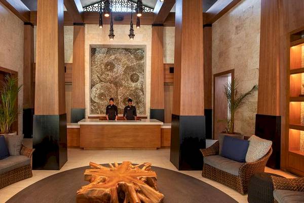 Hotellobby mit Holzelementen, modernen Möbeln, einem großen Holztisch und zwei Mitarbeitern hinter einer Rezeption.