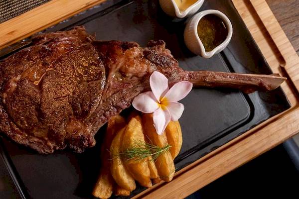 Ein gegrilltes Steak mit Rosmarin und Blumen auf einem schwarzen Teller.