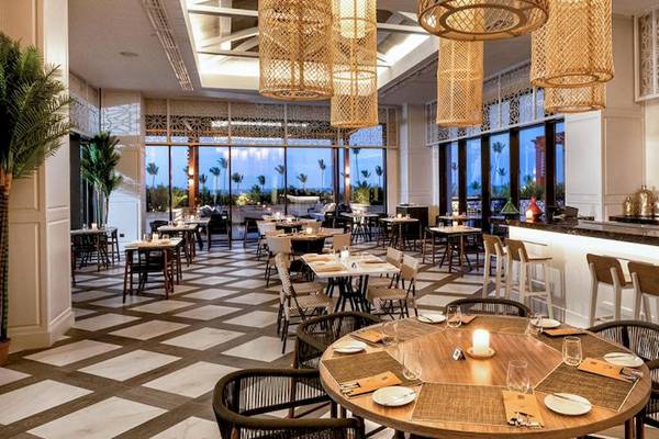 Innenbereich des Lopesan Costa Bavaro Resort Spa & Casino mit Tisch, Stühlen, Bar und Fenstern.