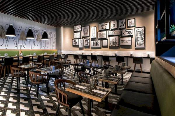 Innenansicht des Restaurants im Lopesan Costa Bavaro Resort Spa & Casino mit schwarzen und weißen Fliesenboden, gerahmten Bildern an der Wand und hängenden Lampen.