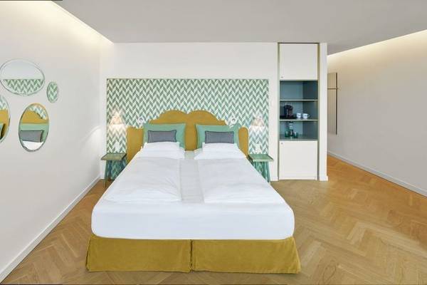 Schlafzimmer im MAXX by Steigenberger Vienna Hotel mit grüner Wand, Bett, Kissen, Nachttischen und Spiegeln.