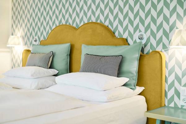 Bett im Hotelzimmer mit grüner und weißer Mustertapete und gelbem Kopfteil