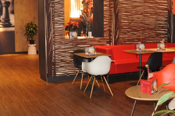 Innenbereich des Ibis Wien Mariahilf Hotels mit Holzboden, roter Couch und runden Tischen.