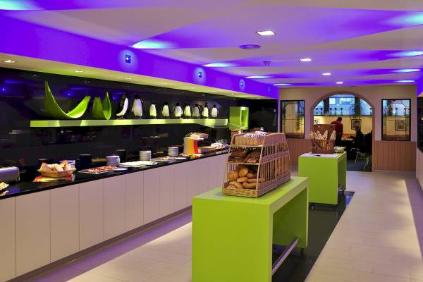 Frühstücksbuffet im Ibis Wien Mariahilf mit grünen Tischen und lila Beleuchtung.