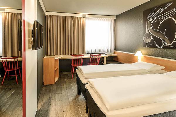 Innenansicht eines Doppelzimmers im Ibis Wien Mariahilf mit zwei Betten, Schreibtisch und Stühlen.