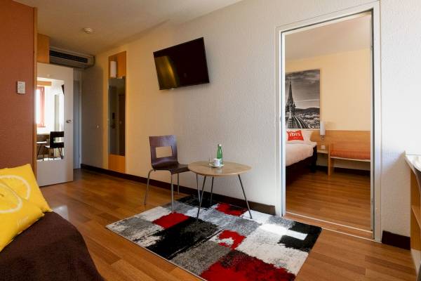 Innenansicht eines Zimmers im Ibis Wien Mariahilf Hotel mit Tisch, Stühlen und Fernseher an der Wand.