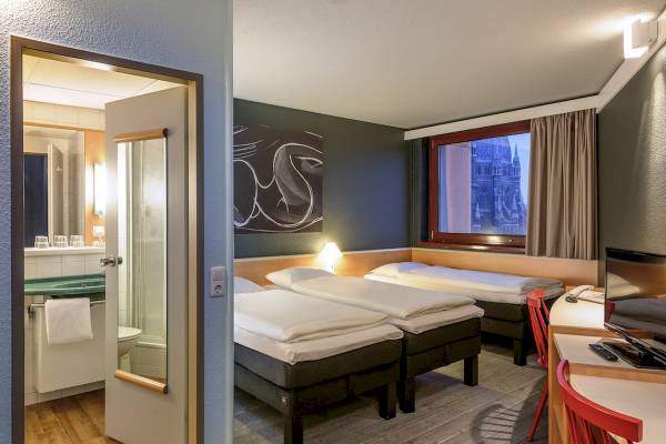 Hotelzimmer im Ibis Wien Mariahilf mit drei Betten und Stadtblick.