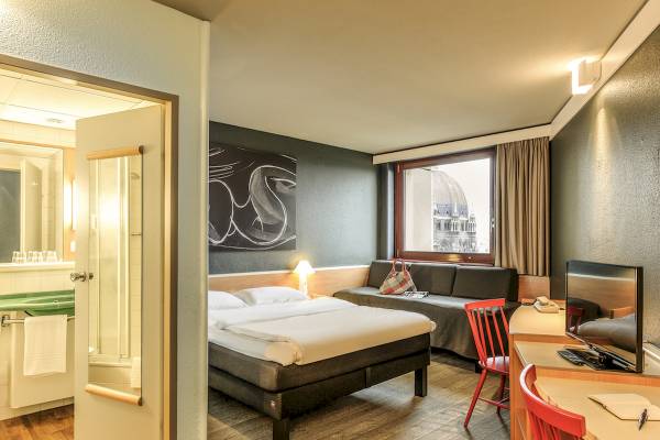 Innenansicht eines Zimmers im Ibis Wien Mariahilf Hotel mit Doppelbett, Sofa, Schreibtisch und Fernseher.