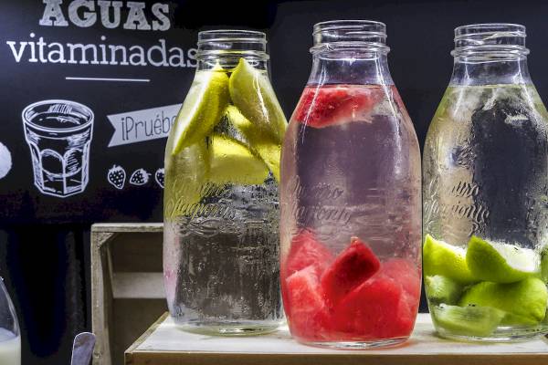 Drei Gläser mit Wasser und Fruchtscheiben, eines mit Gurkenscheiben, eines mit Wassermelonenscheiben und eines mit Limettenscheiben.