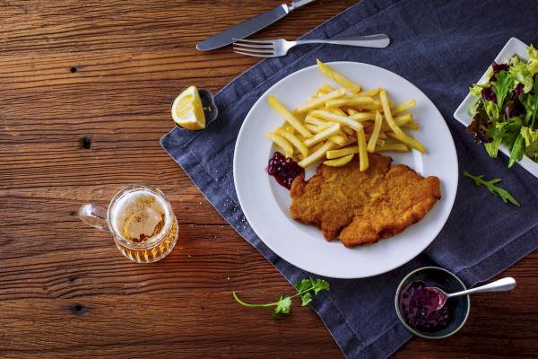 Teller mit Schnitzel, Pommes und Salat auf einem Holztisch mit Glas Bier, Ibis Wien Mariahilf