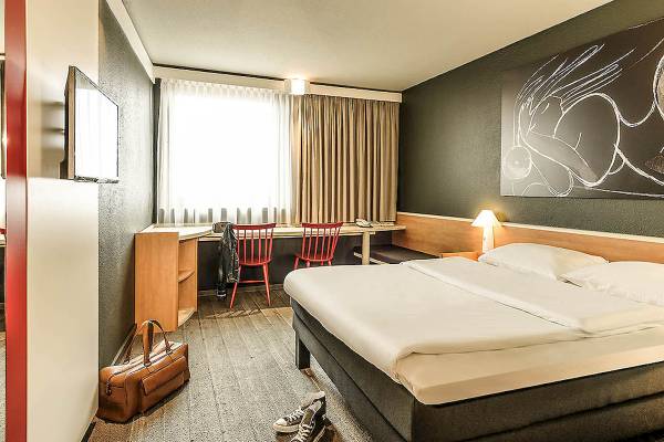 Hotelzimmer im Ibis Wien Mariahilf mit Doppelbett, Schreibtisch, Stühlen und Gemälde an der Wand.