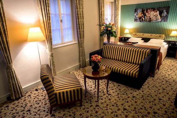 Schlafzimmer im Mercure Grand Hotel Biedermeier mit Bett, Sofa, Tisch und Blumenvase.